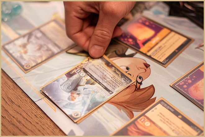 A hand is placing a Disney Lorcana Trading Card Game card on a table