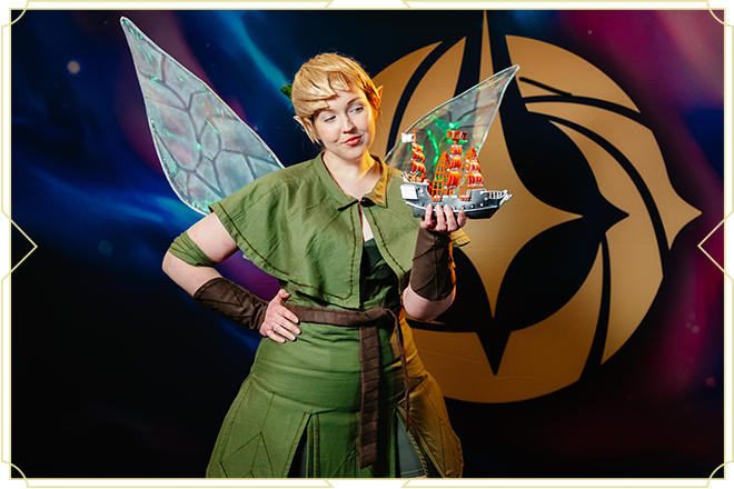 Young woman dressed as Tinker Bell holding a pirate ship toy.